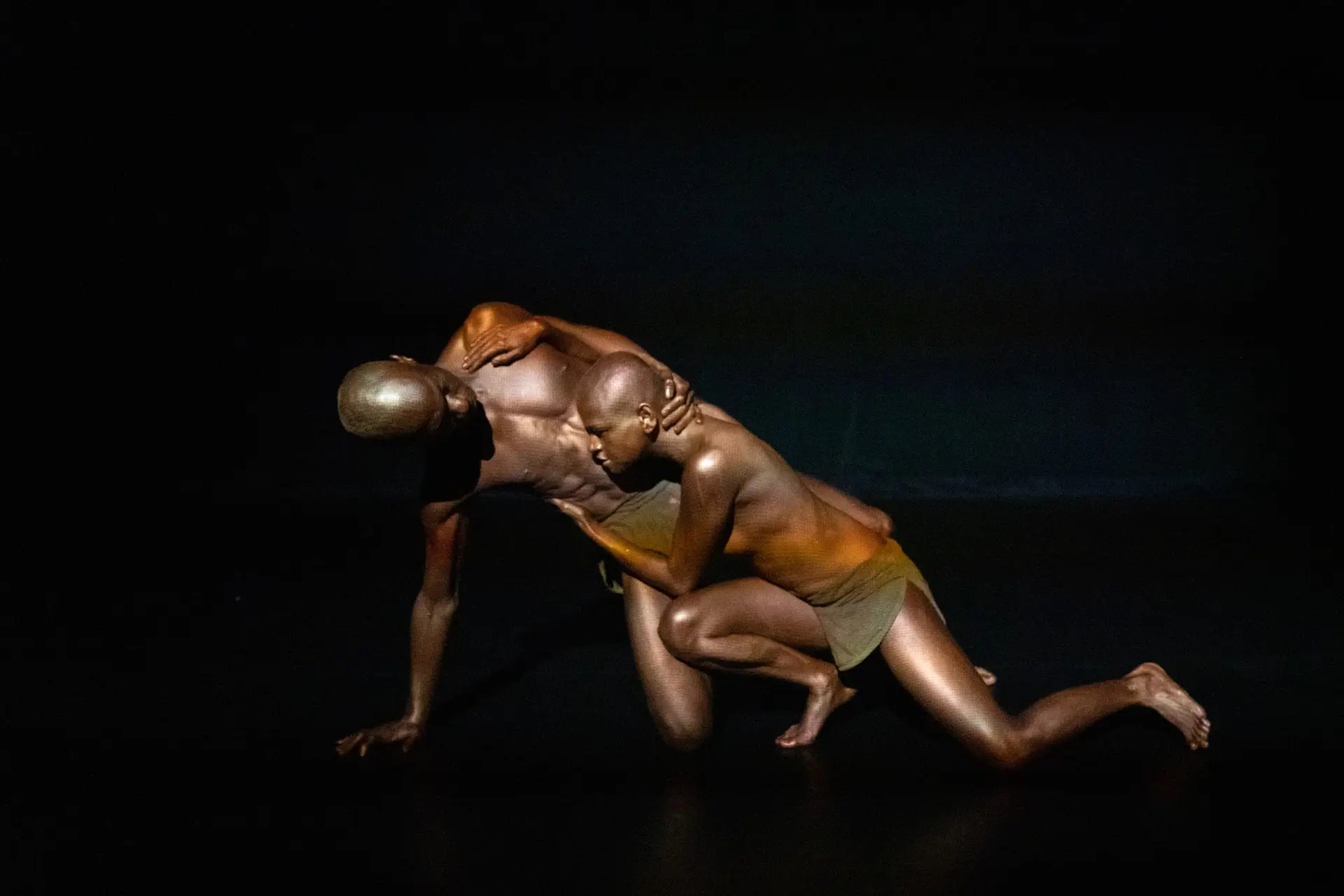 Mirelle Martins and Shamel Pitts entwined in bronze body paint on a black stage in BLACK VELVET